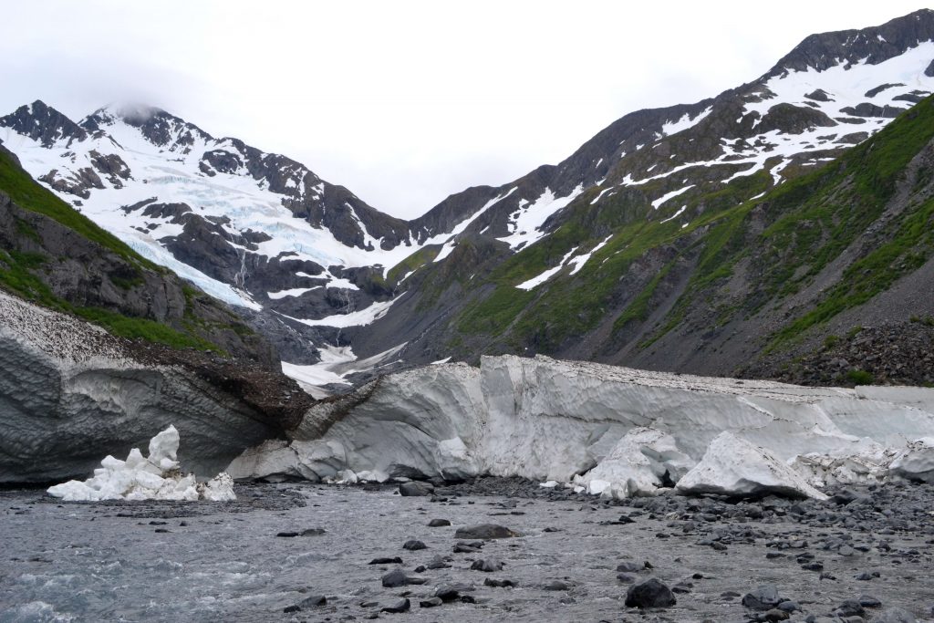 Ustupujúci ľadovec Byron a riečka pretínajúca snehové polia z lavín napadaných z okolitých kopcov

